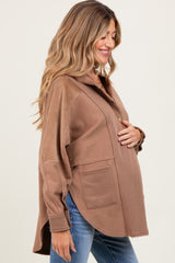 woman wearing a brown maternity pullover with a collar and pockets, gently cradling her baby bump