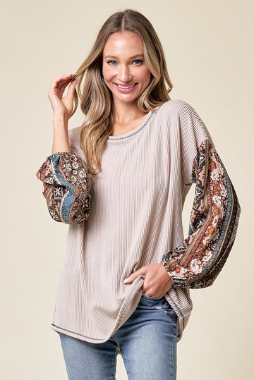 woman wearing a beige long sleeve top with patterned floral sleeves and a relaxed fit, posing with a smile