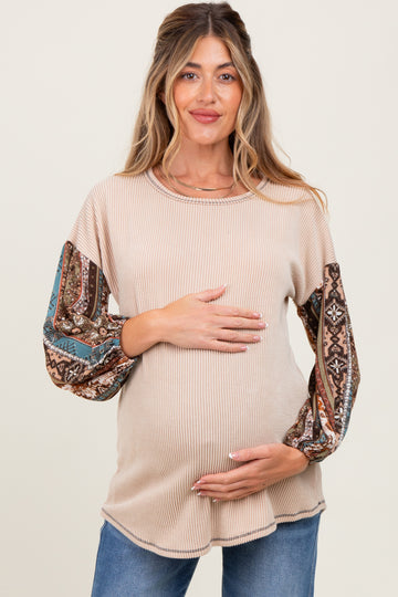 woman wearing a beige ribbed maternity top with patterned long sleeves and holding her baby bump
