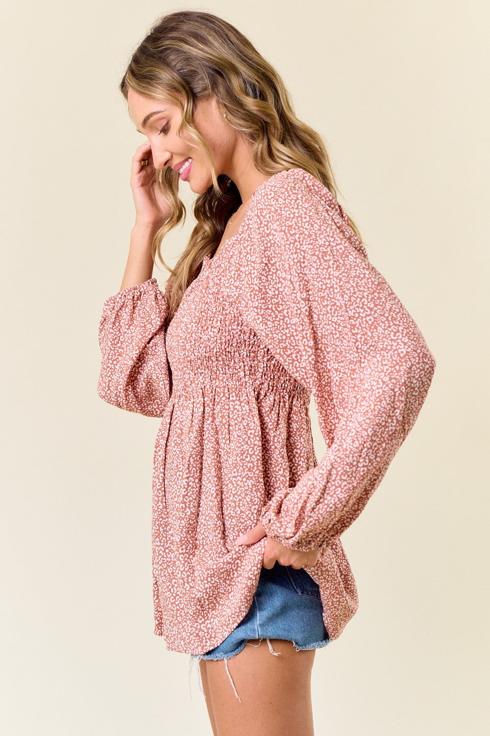 woman wearing a pink floral smocked blouse with long sleeves and a relaxed fit, paired with denim shorts