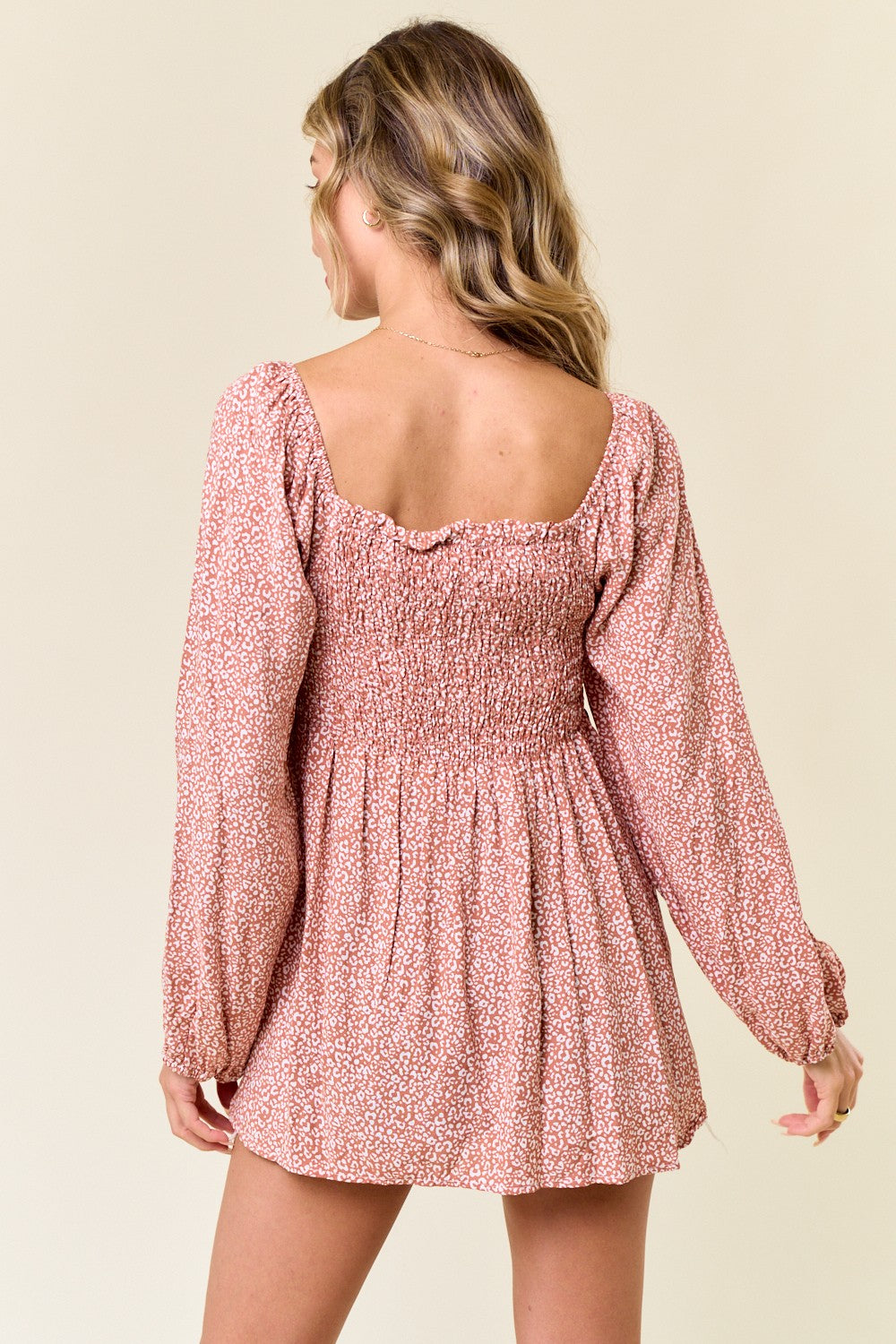 woman wearing a pink floral smocked mini dress with long sleeves and a square neckline, view from the back