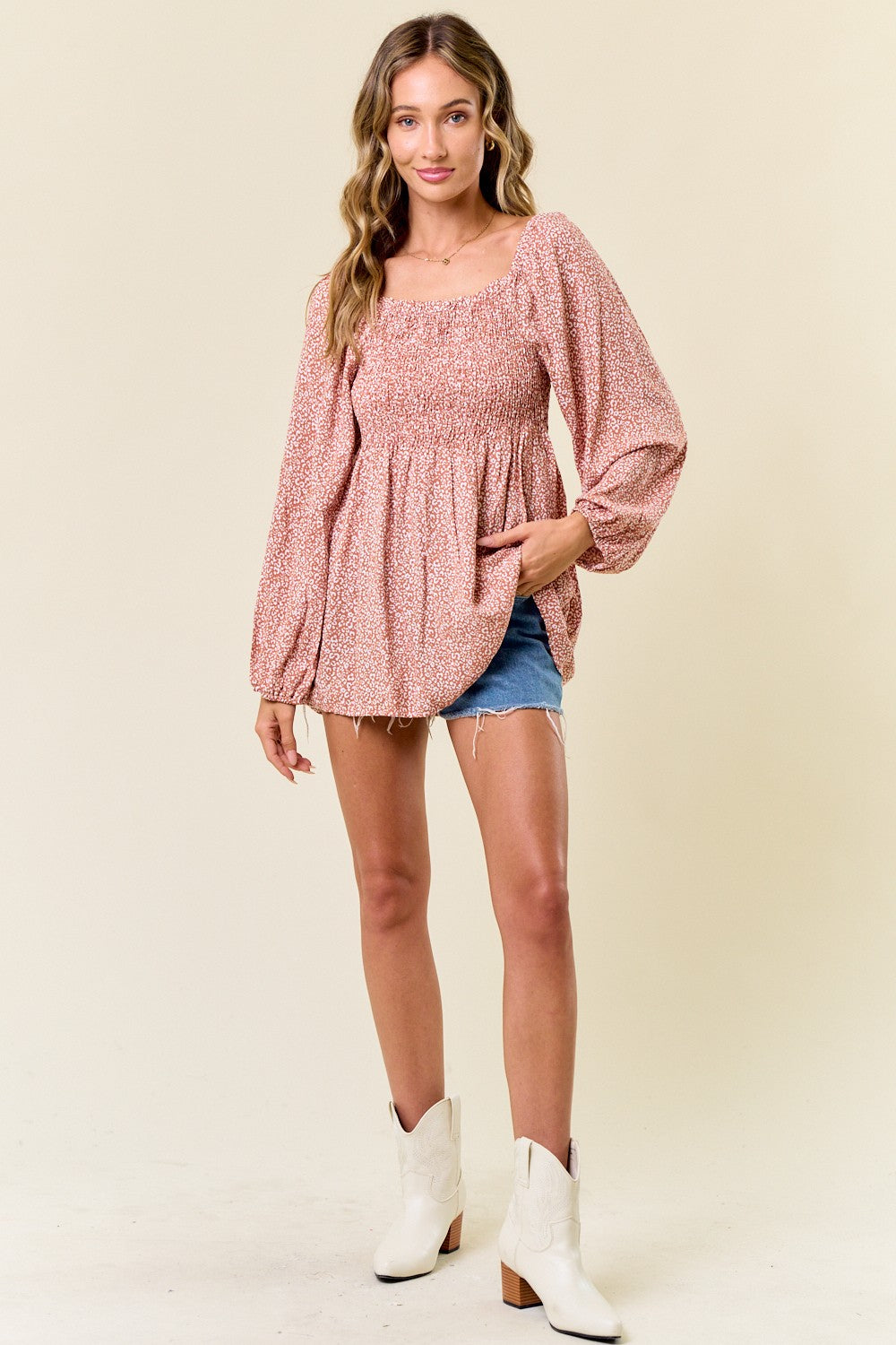 woman wearing a pink floral smocked blouse with puff sleeves paired with denim shorts and white ankle boots