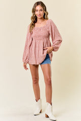 woman wearing a pink floral smocked blouse with puff sleeves paired with denim shorts and white ankle boots