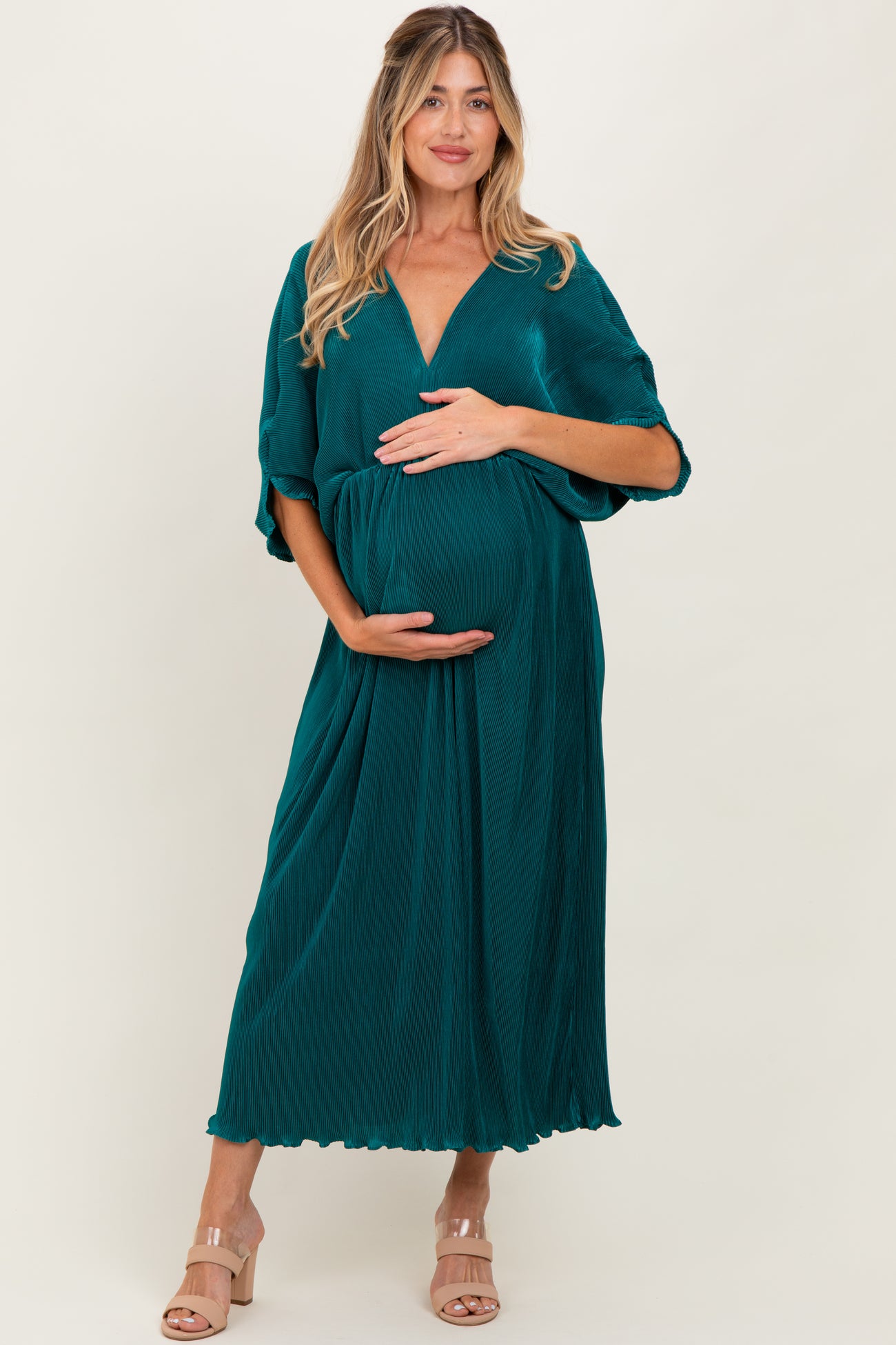 woman wearing a teal maternity maxi dress with short sleeves, gently cradling her baby bump