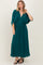 woman wearing a teal maxi dress with a v-neck and short dolman sleeves, standing against a neutral background