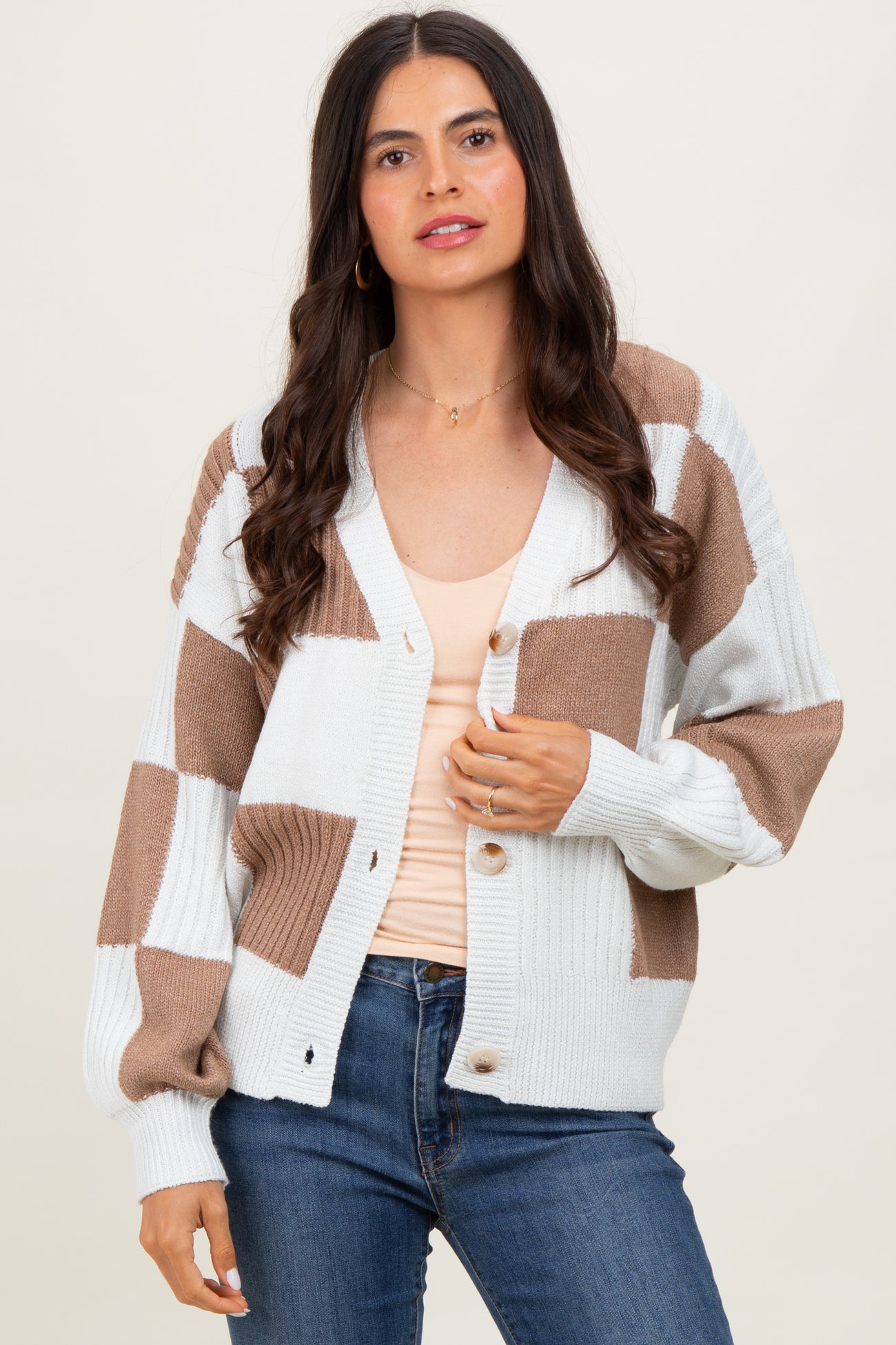woman wearing a cream and brown checkered oversized cardigan over a beige top and blue jeans