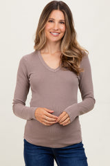woman wearing a taupe long sleeve maternity top with a v-neck and holding her baby bump