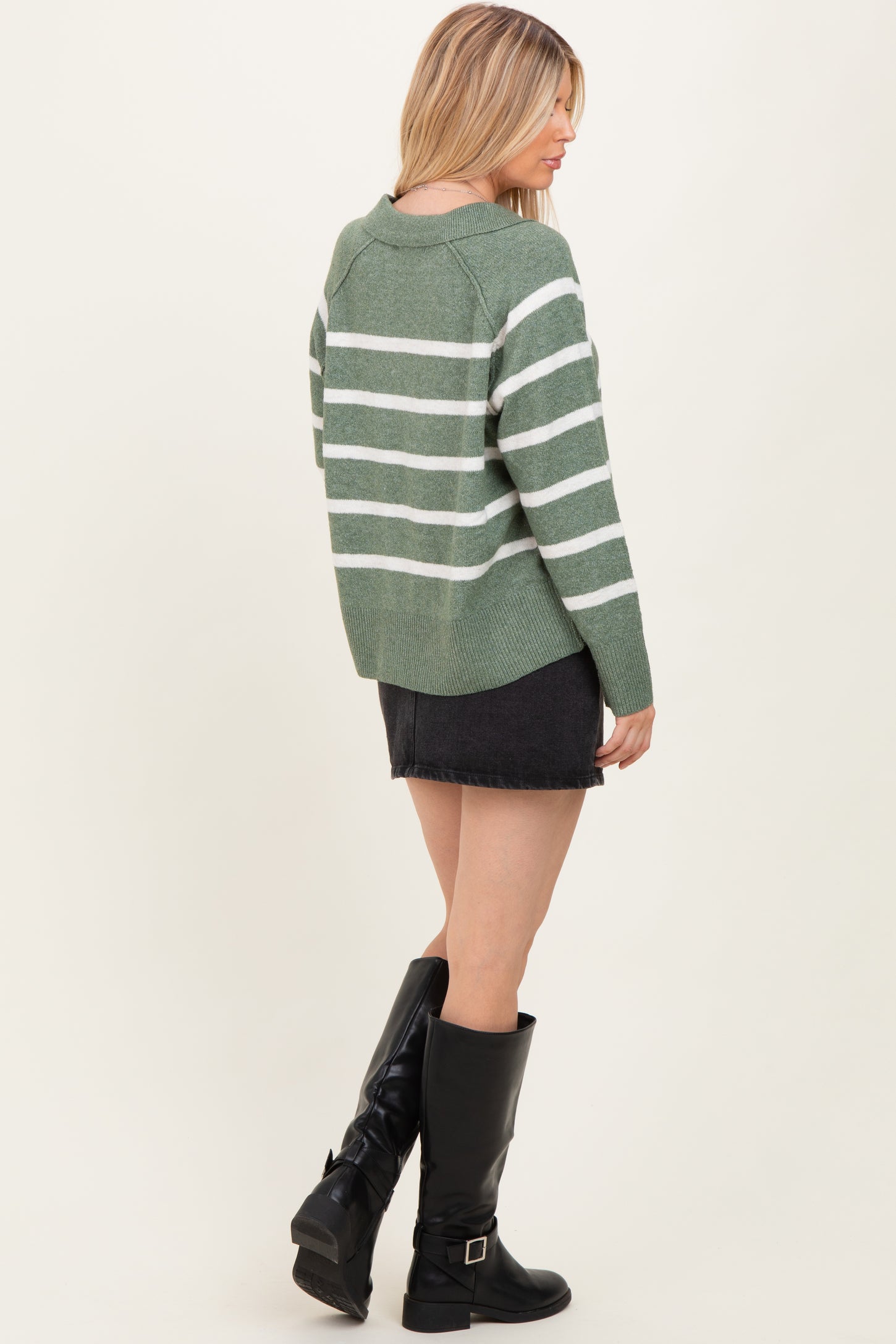 woman wearing a green striped sweater with white stripes and a black denim skirt, paired with knee-high black boots
