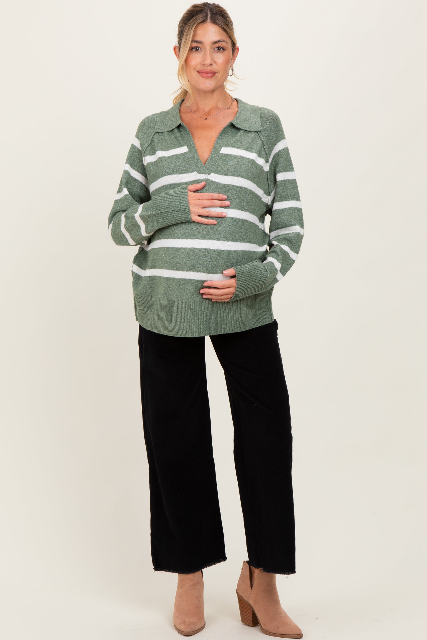 woman wearing a green and white striped maternity sweater and black wide-leg pants, holding her baby bump
