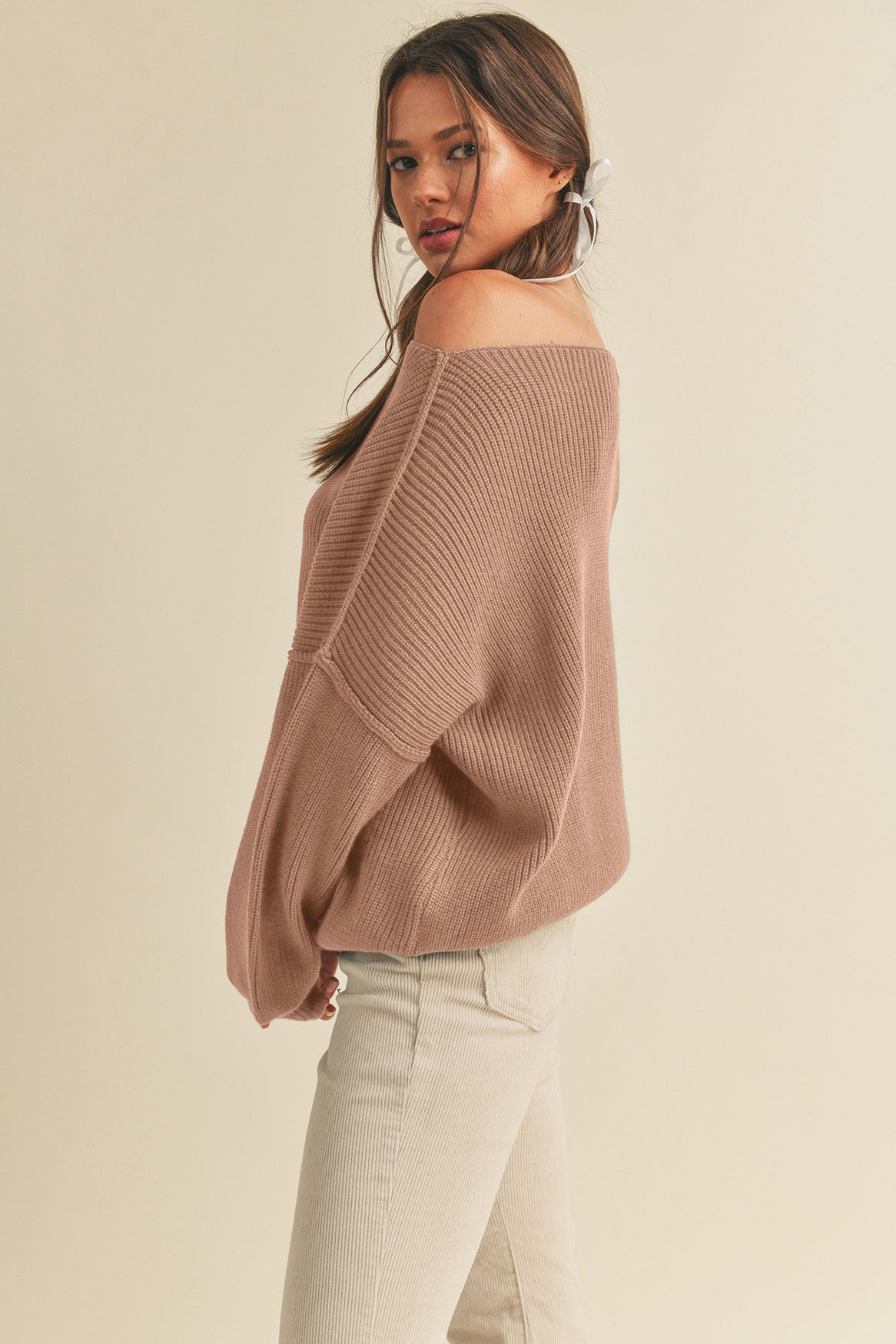 woman wearing a oversized off-the-shoulder ribbed sweater in dusty rose color with light beige high-waisted pants