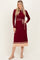 woman wearing a burgundy ribbed long sleeve dress with a tie belt and a beige pleated hem