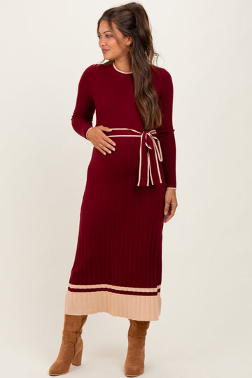 woman wearing a burgundy ribbed maternity dress with a belted waist and contrasting cream-colored stripes, showing her baby bump