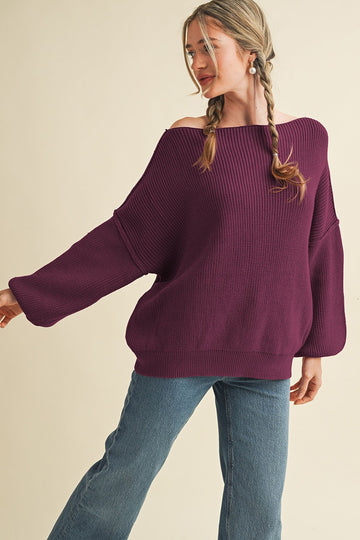 woman wearing a purple off-the-shoulder oversized sweater with ribbed texture and wide sleeves, paired with jeans