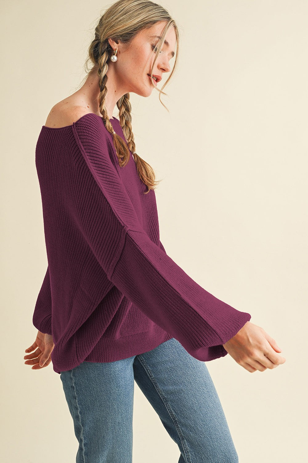 woman wearing a deep purple off-the-shoulder knit sweater with wide sleeves and paired with blue jeans