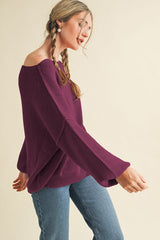woman wearing a deep purple off-the-shoulder knit sweater with wide sleeves and paired with blue jeans
