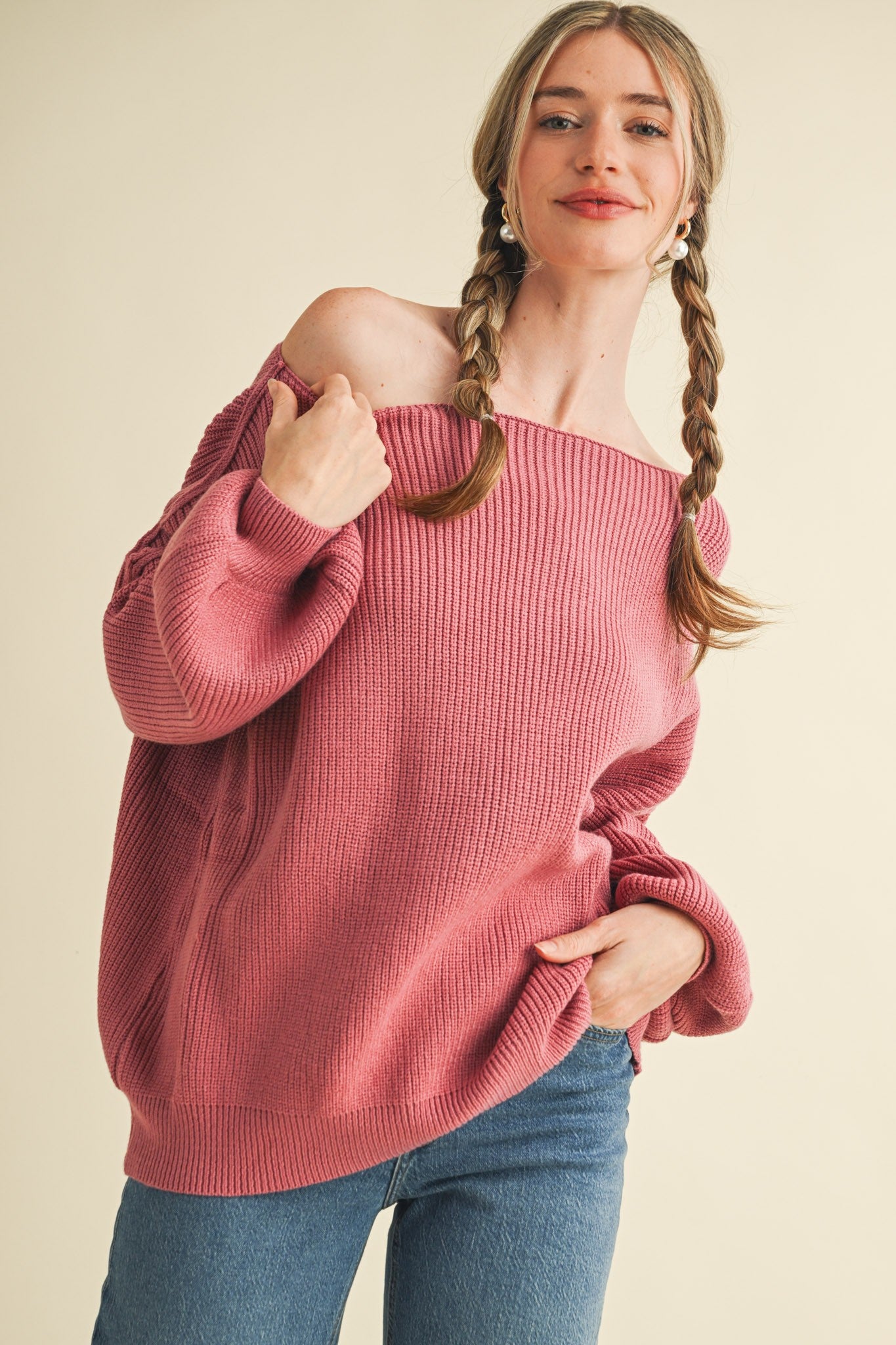 woman wearing a pink off-the-shoulder sweater with a ribbed texture and styled with playful braids