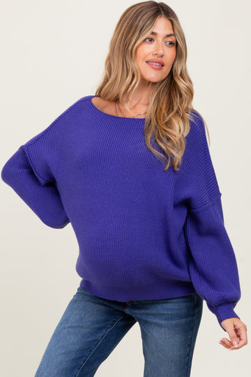 woman wearing a purple oversized knit maternity sweater and showing her baby bump with blue jeans
