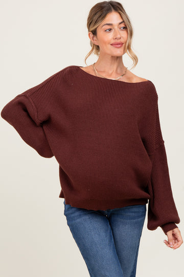woman wearing a dark brown oversized knit maternity sweater and fitted jeans, with a relaxed fit and boat neckline