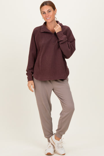 woman wearing a maroon fleece pullover with a collar and buttons, paired with gray jogger pants and white sneakers