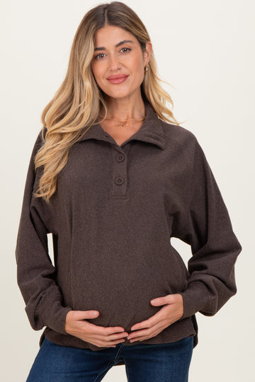 woman wearing a dark brown maternity pullover with buttons and a relaxed fit, holding her baby bump