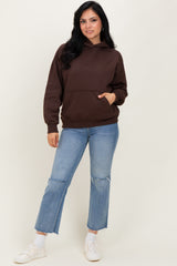 woman wearing a brown hooded sweatshirt with a front pocket and light blue ripped flared jeans