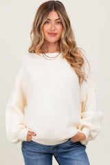 woman wearing a cream oversized maternity sweater with ribbed texture and balloon sleeves, smiling and posing with hands in pockets