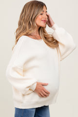 woman wearing a cream oversized ribbed maternity sweater and holding her baby bump