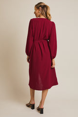 woman wearing a burgundy long sleeve dress with a tie belt and a midi length, showing the back view