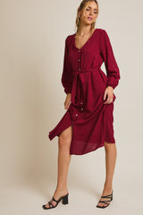woman wearing a burgundy button-down midi dress with long sleeves and a tied waist, paired with black strappy heels
