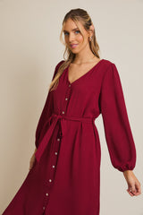 woman wearing a burgundy button-up dress with a v-neck and long puff sleeves, cinched at the waist with a tie belt