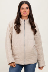 woman wearing a tan quilted zip-up jacket with a high collar and blue jeans