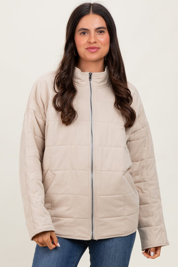 woman wearing a tan quilted zip-up jacket with a high collar and blue jeans