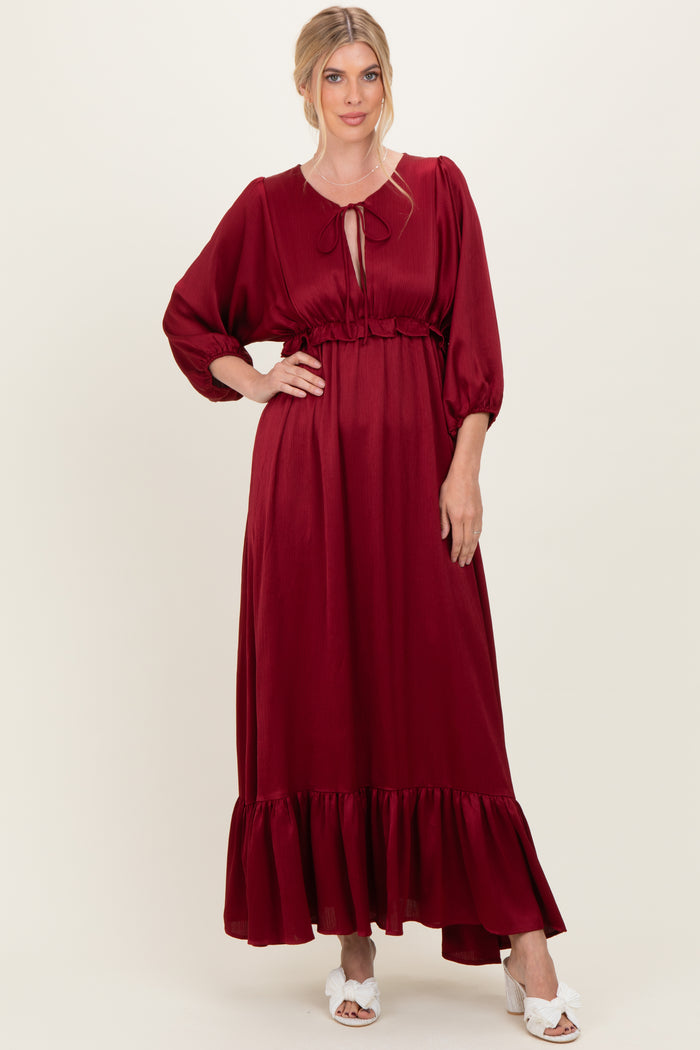 woman wearing a burgundy maxi dress with puff sleeves and a ruffled hem, styled with a tie neckline and white sandals