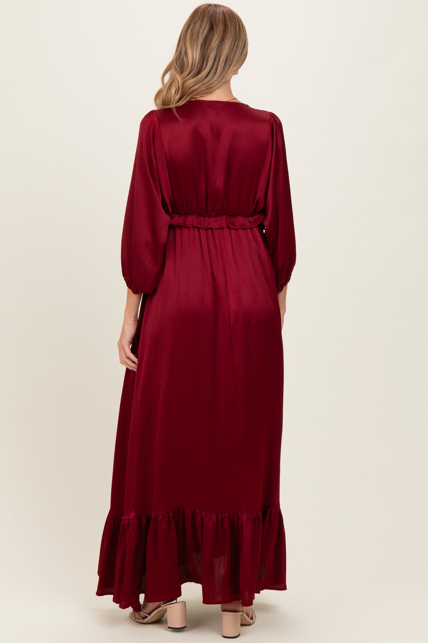 woman wearing a burgundy long sleeve maternity dress with a ruffled hem and belted waist, showing her baby bump
