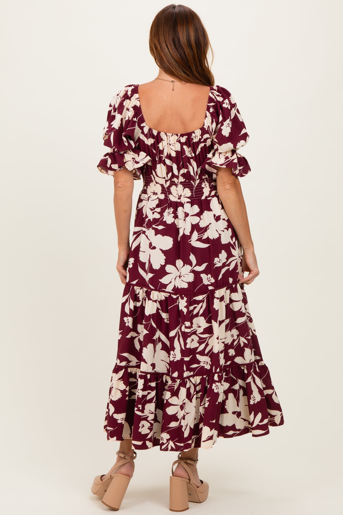 woman wearing a maroon floral maxi dress with puff sleeves and a tiered skirt, viewed from the back