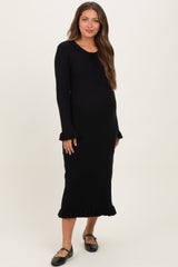 woman wearing a black maternity ribbed dress with a tie neckline and ruffled sleeves, showing her baby bump