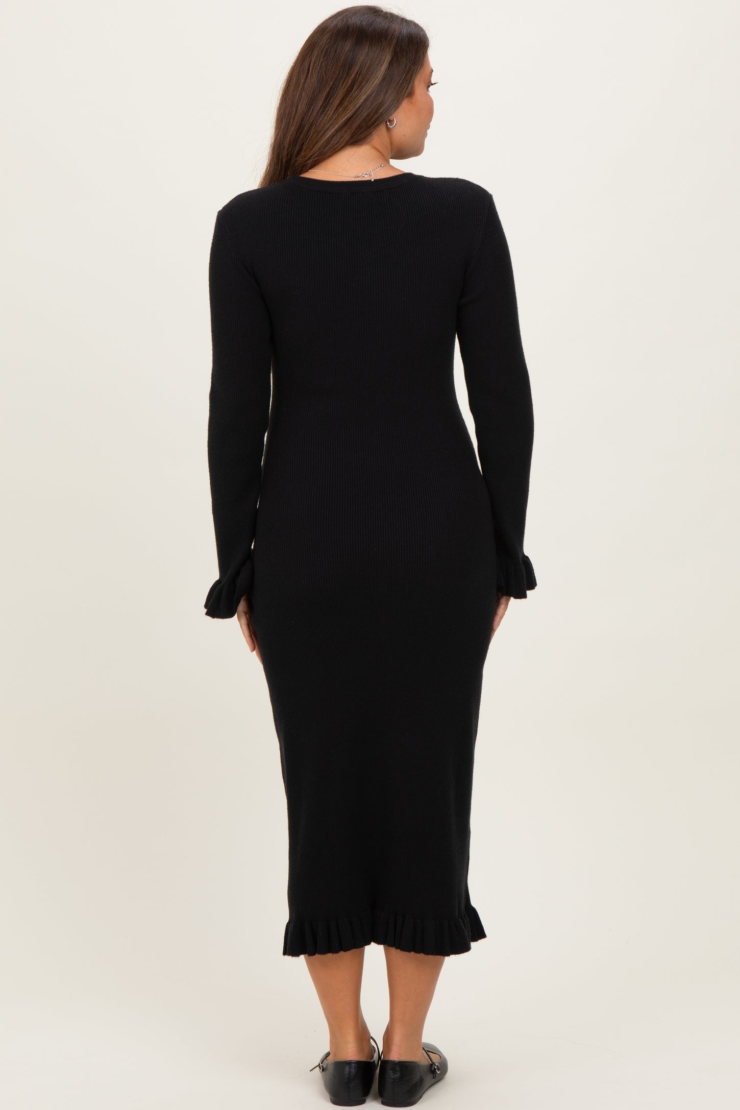 woman wearing a black ribbed maternity dress with long sleeves and ruffled hem, seen from the back