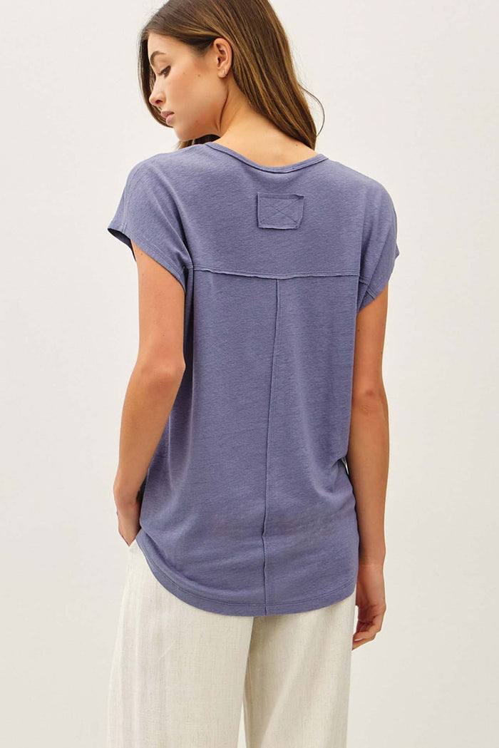 woman wearing a relaxed fit purple short sleeve top with a back pocket detail and light-colored wide leg pants