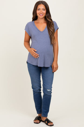 woman wearing a slate blue maternity top and distressed jeans, holding her baby bump