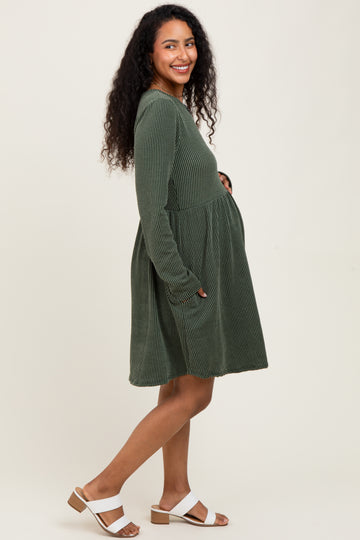 woman wearing a dark green striped maternity dress with long sleeves and pockets, showing her baby bump