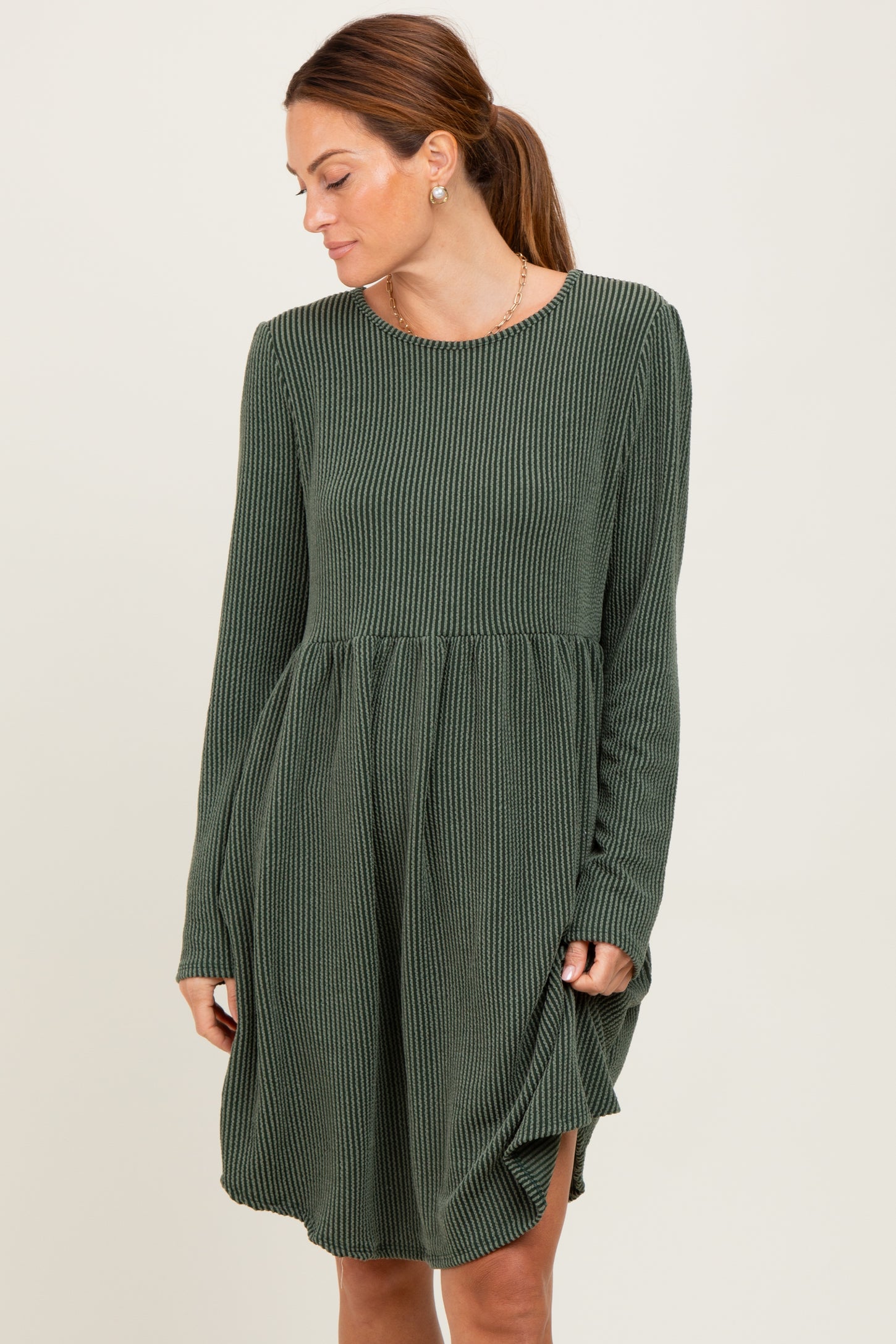 woman wearing a dark green long sleeve striped dress with a relaxed fit and gathered waist