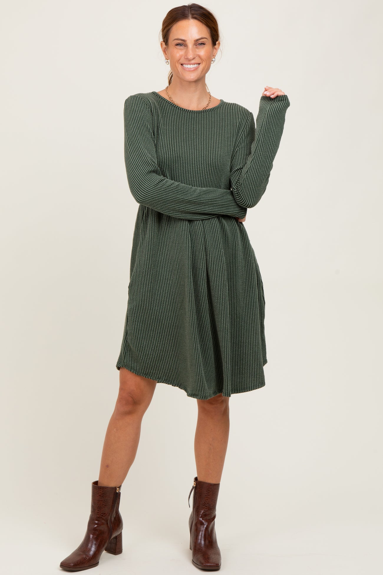 woman wearing a green striped long sleeve dress and brown ankle boots, posing with one hand on her hip