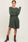 woman wearing a green striped long sleeve dress and brown ankle boots, posing with one hand on her hip