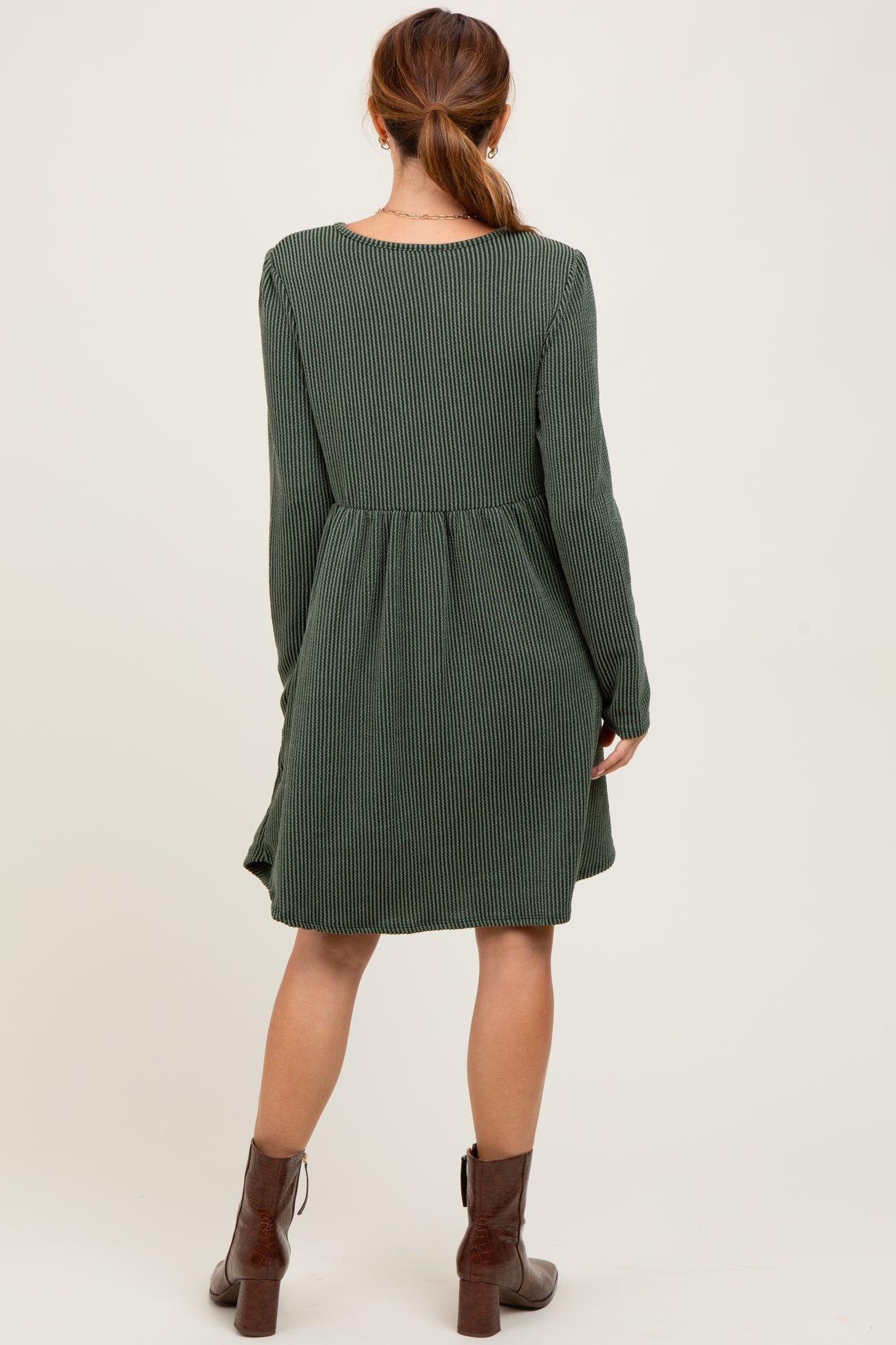 woman wearing a green ribbed long sleeve dress with a loose fit and a flared hem, viewed from the back