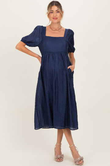 woman wearing a navy blue puff sleeve maternity dress with square neckline and pockets, showcasing her baby bump