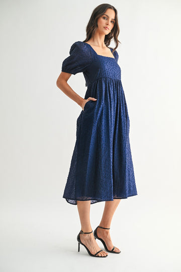 woman wearing a navy blue midi dress with short puff sleeves and pockets, styled with strappy black heels