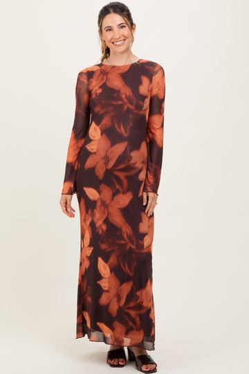 woman wearing a long sleeve maternity dress with an orange floral print on a dark background, standing and smiling