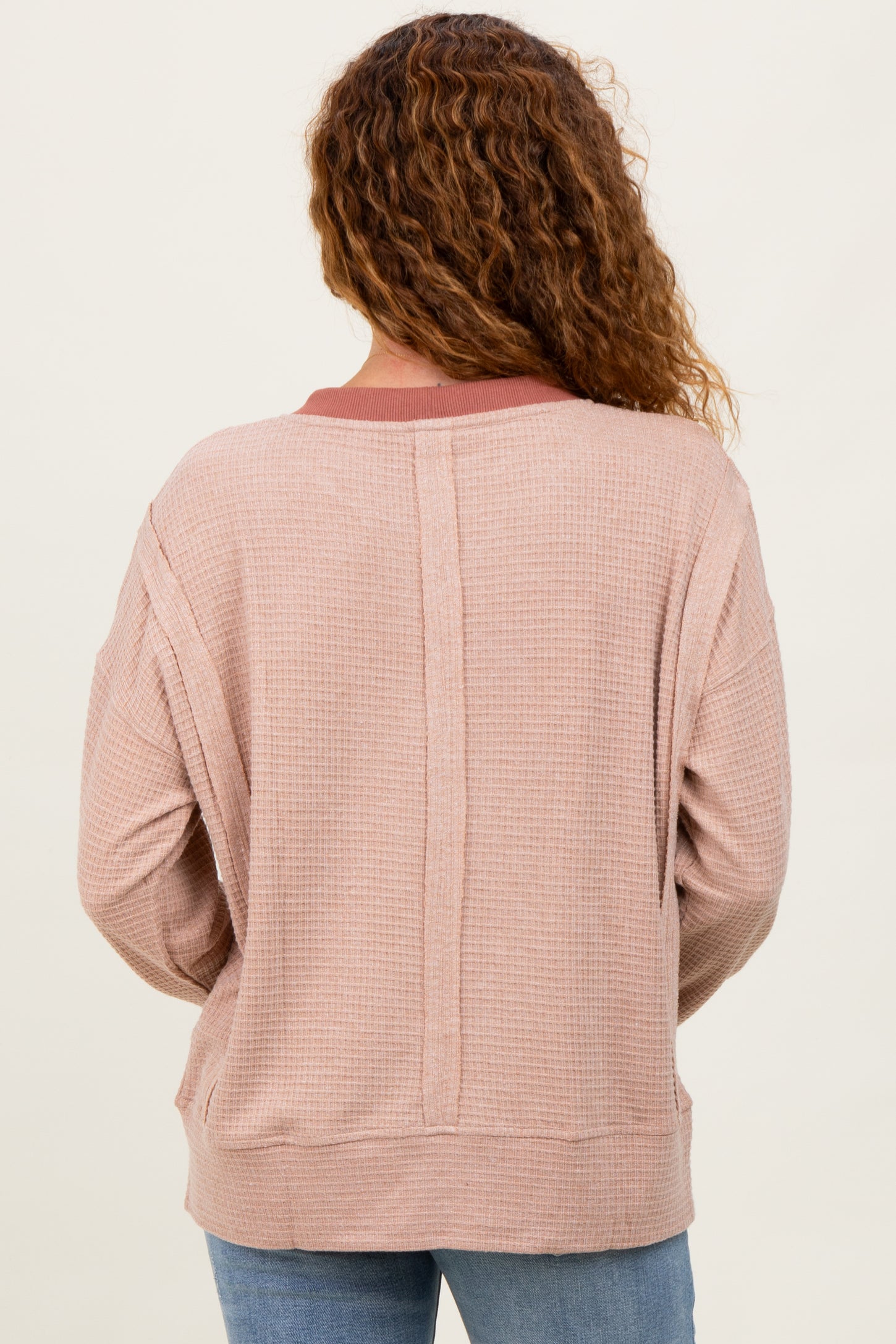 woman wearing a light pink waffle knit top with a relaxed fit and contrasting neckline detail, viewed from the back