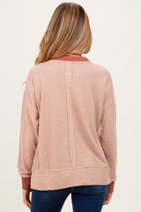 woman wearing a light pink maternity pullover with a slightly textured fabric and contrasting burgundy collar, seen from the back