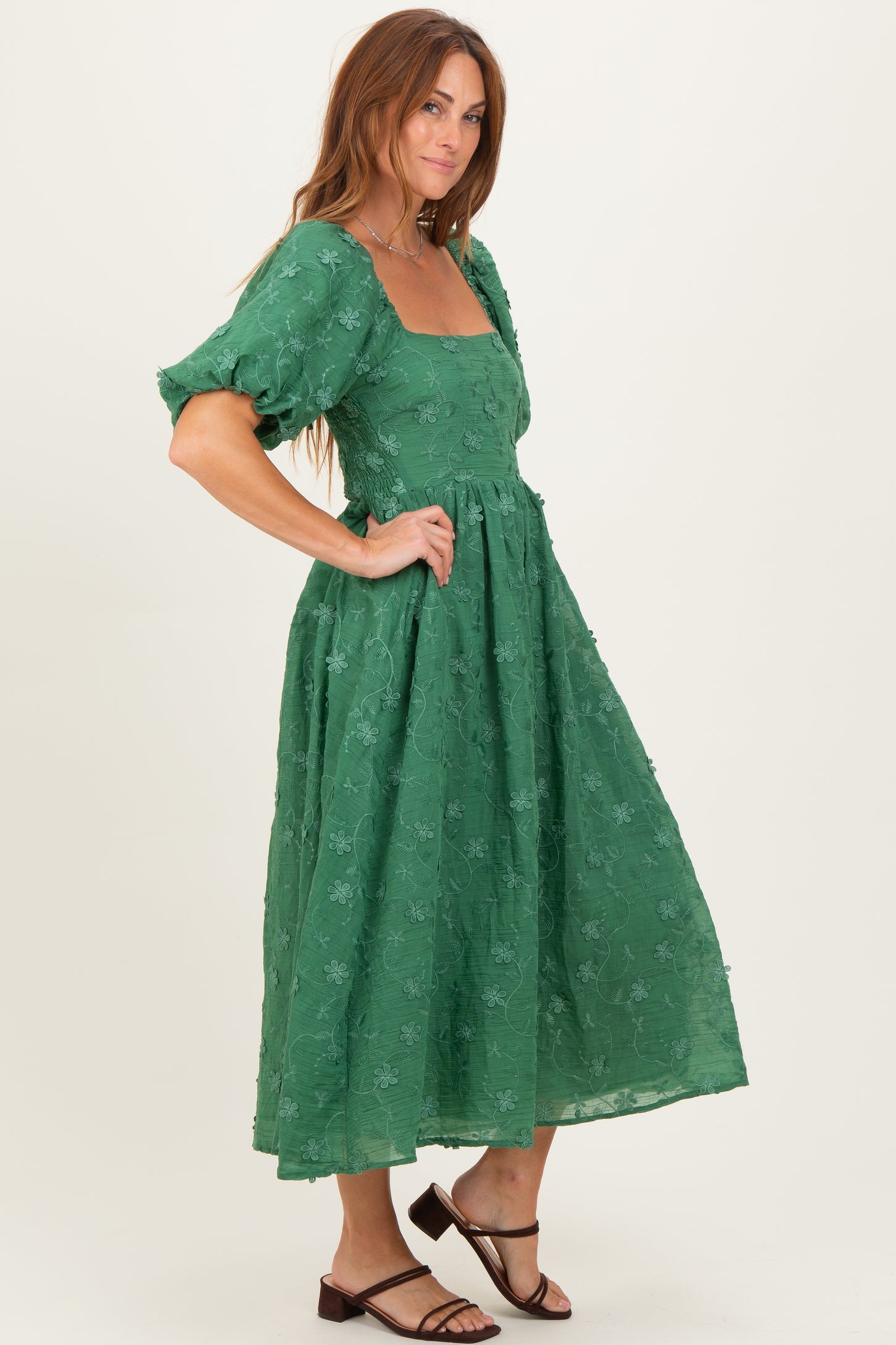 woman wearing a green midi dress with puff sleeves and floral embroidery, standing in profile